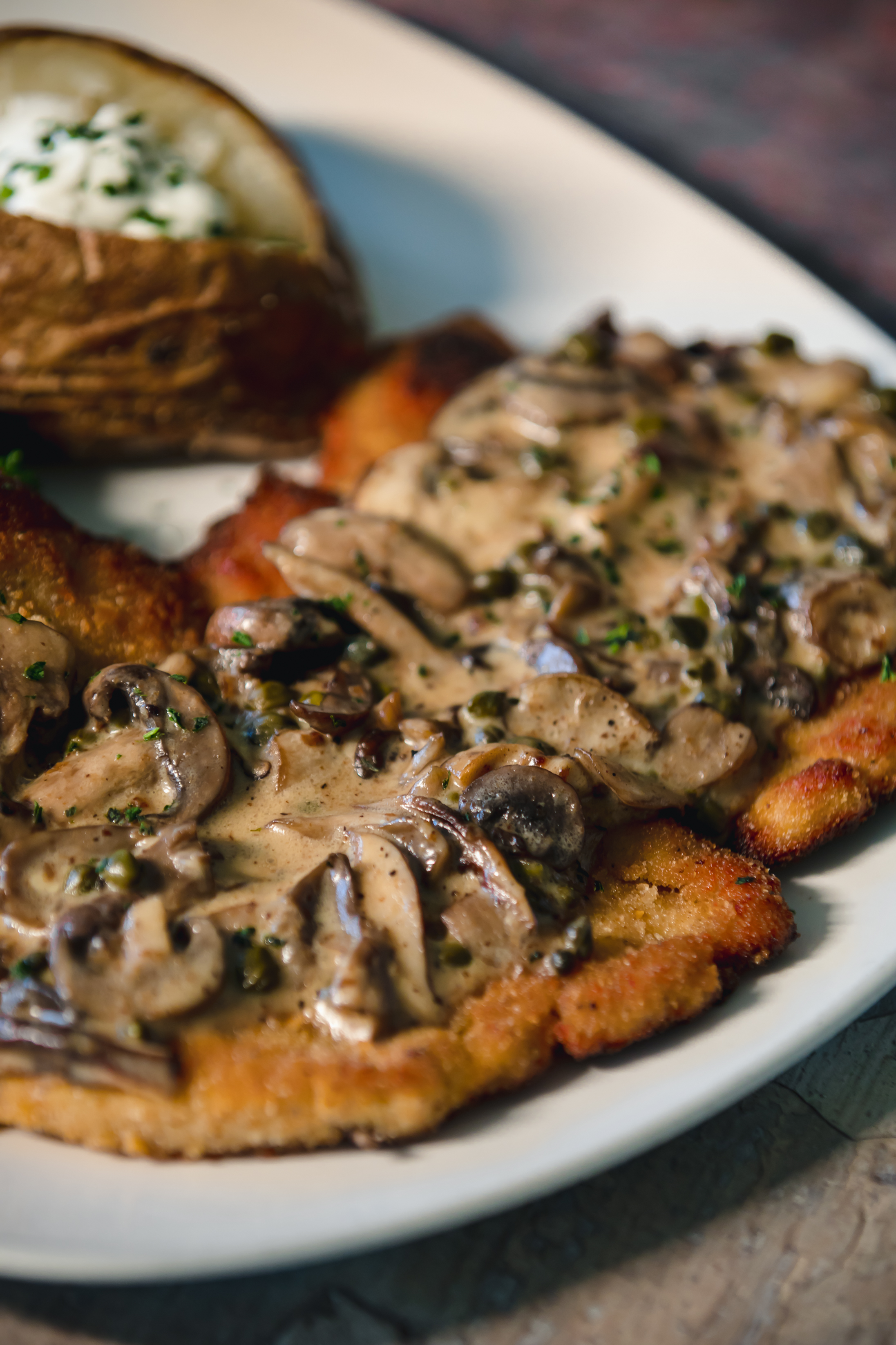 Jaeger Schnitzel. Tender Pork Loin Cutlet, Mushrooms. White Wine Lemon Caper Sauce, baked potato
